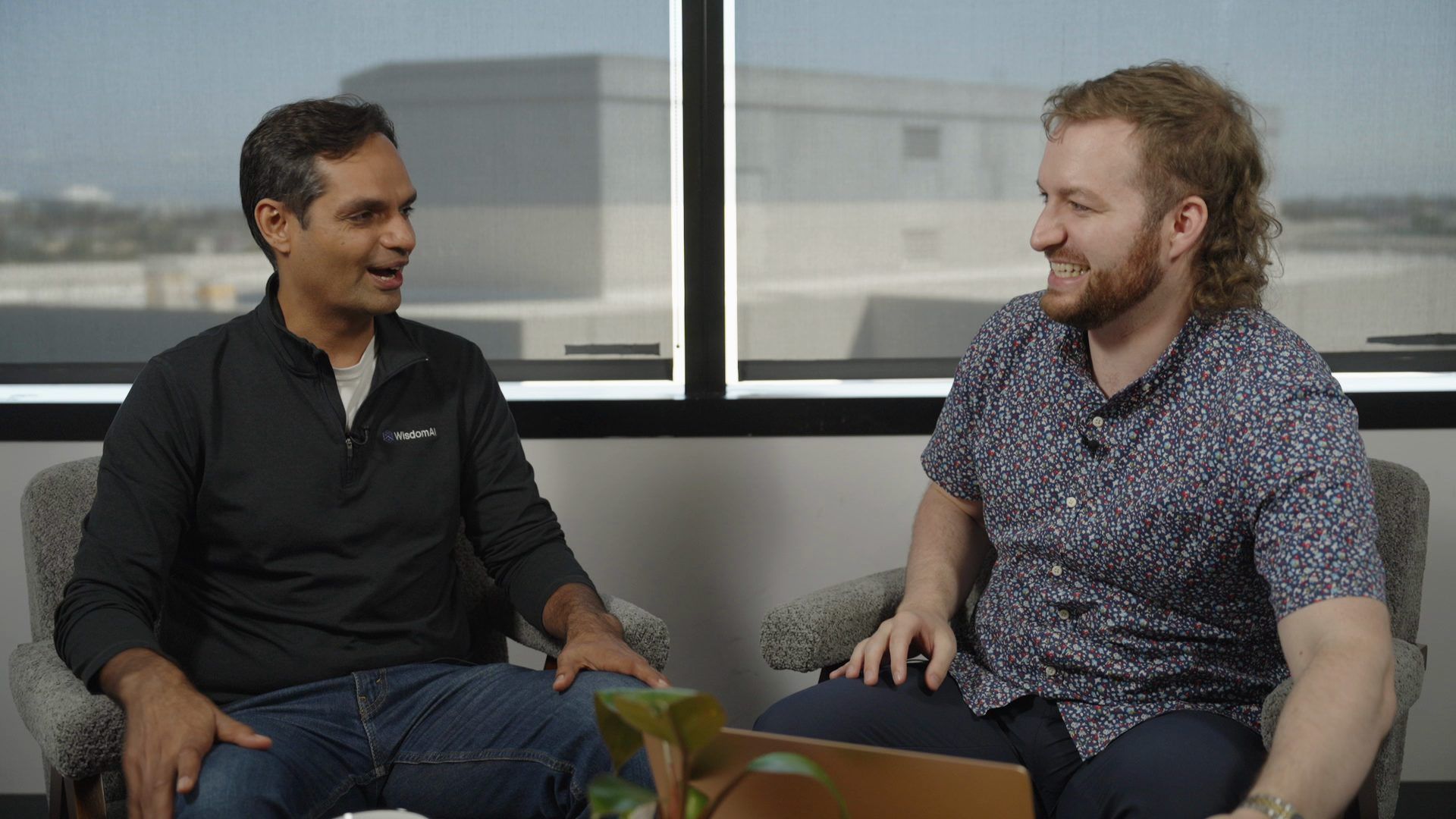 Conor Bronsdon and Kapil Chhabra laughing mid-conversation in armchairs by a sunlit window during a Chain of Thought recording